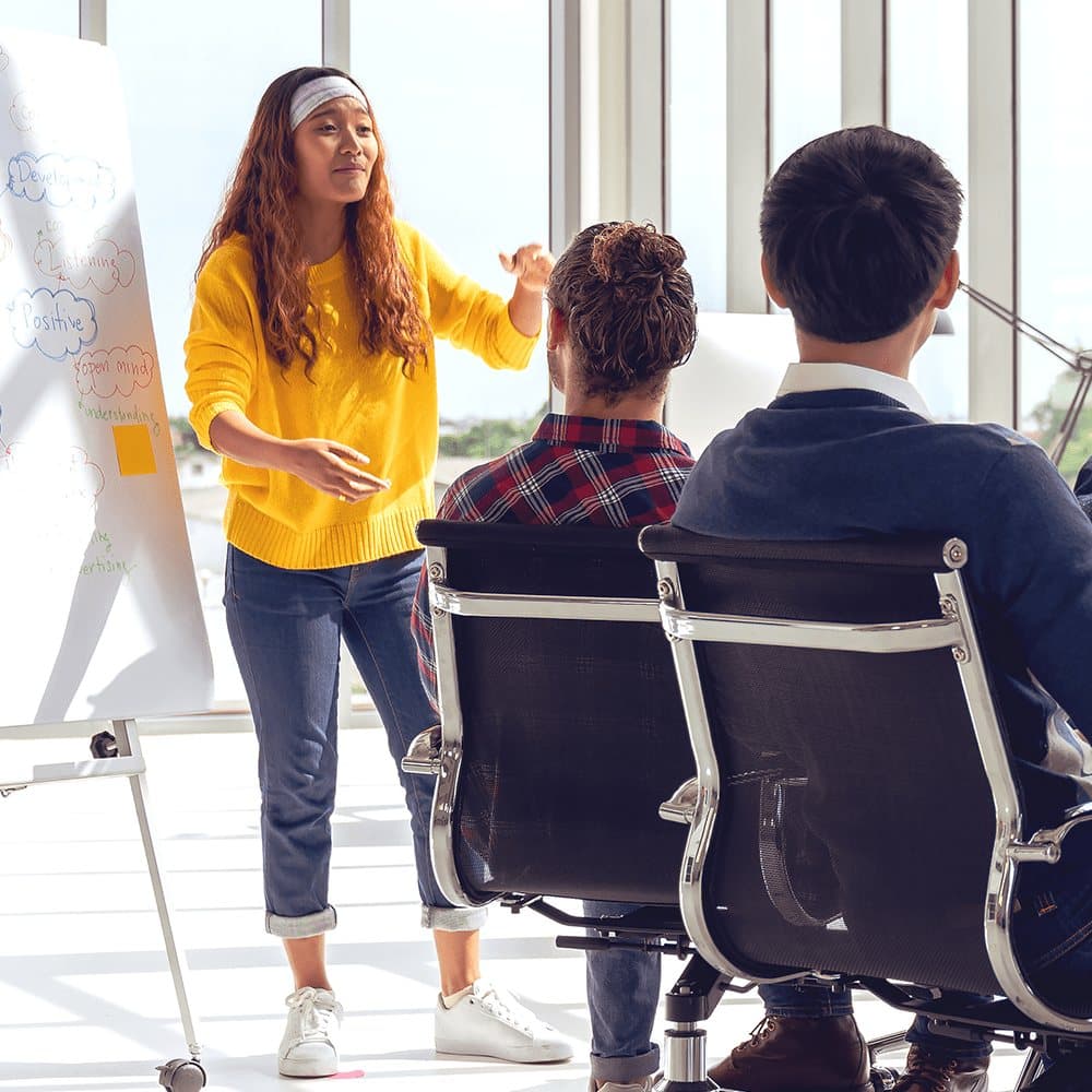 A facilitator presenting at a whiteboard to a seated team.